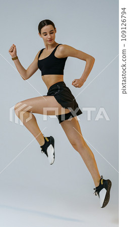 Pretty sporty woman running in Mid-Air exercising during cardio workout over studio background 109126794