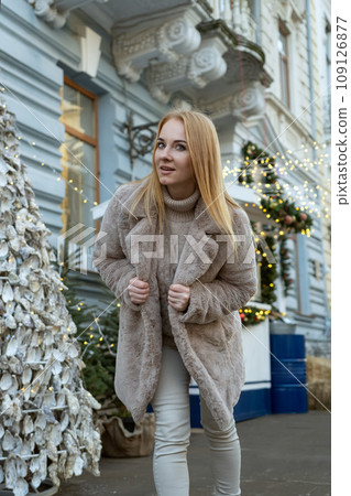 Attractive young blond woman in a fur coat standing on a city street. Christmas festive atmosphere. Vertical frame 109126877