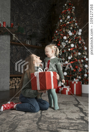 Portrait of mom and her cute daughter with Xmas presents near Christmas tree. Mother and little girl with New Year decorations. Portrait of mom and her cute daughter with Xmas presents near Christmas tree. Mother and little girl with New Year decorations. 109127168