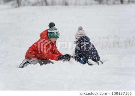 Siblings are played outside in the winter. Two children sit in the snow on frosty day. Winter holidays 109127195