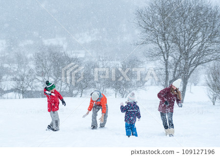 Big family with children play snowballs outside during snowfall. Winter fun holidays. Games in winter outdoors. 109127196