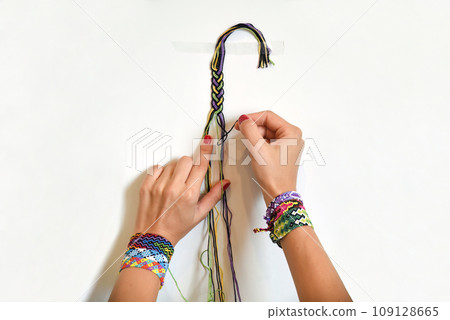 Female hands weaving knot for DIY friendship bracelet Pigtail. Many handmade bracelets on girls wrists. Friendship bracelet making process, step by step. White background with copy space Female hands weaving knot for DIY friendship bracelet Pigtail. Many handmade bracelets on girls wrists. Friendship bracelet making process, step by step. White background with copy space 109128665