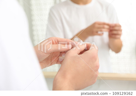 Teen guy using acne healing patch near mirror indoors, focus on hands Teen guy using acne healing patch near mirror indoors, focus on hands 109129162