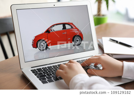 Woman using laptop to buy car at wooden table indoors, closeup Woman using laptop to buy car at wooden table indoors, closeup 109129182