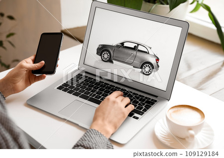 Woman using laptop and phone to buy car at table indoors, closeup Woman using laptop and phone to buy car at table indoors, closeup 109129184