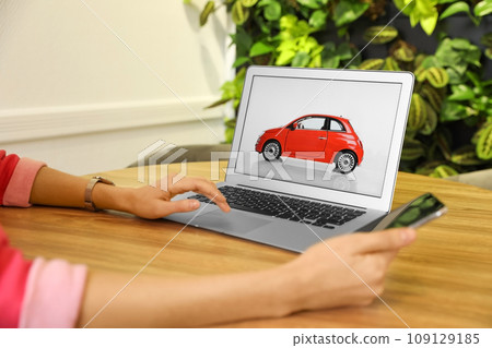 Woman using laptop and phone to buy car at wooden table indoors, closeup Woman using laptop and phone to buy car at wooden table indoors, closeup 109129185