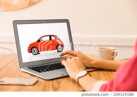 Woman using laptop to buy car at wooden table indoors, closeup Woman using laptop to buy car at wooden table indoors, closeup 109129186