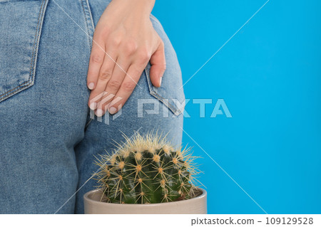 Woman sitting down on cactus against light blue background, space for text. Hemorrhoid concept 109129528