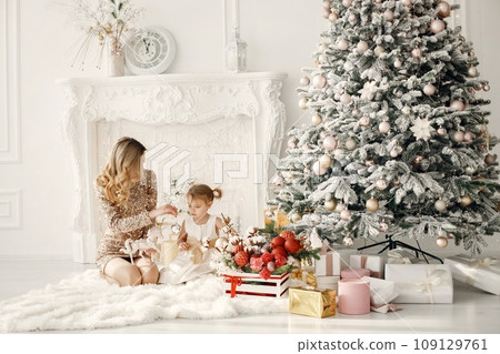 Blonde mother and little daughter in studio posing for a photo. Woman wearing golden dress and daughter white one. Family decorating Christmas together. 109129761