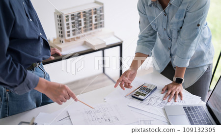 Two engineer architect pointing on blueprint of sketching interior architectural building to discussion technical for construction plan and building model while working together in workplace site 109132305