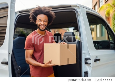 Young African American man holds cardboard box with packaged goods making home delivery. 109133333
