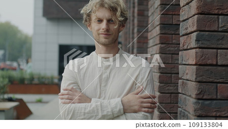 Slow motion portrait of confident person standing in city street next to office building smiling looking at camera. Modern youth and positive emotion concept. Slow motion portrait of confident person standing in city street next to office building smiling looking at camera. Modern youth and positive emotion concept. 109133804