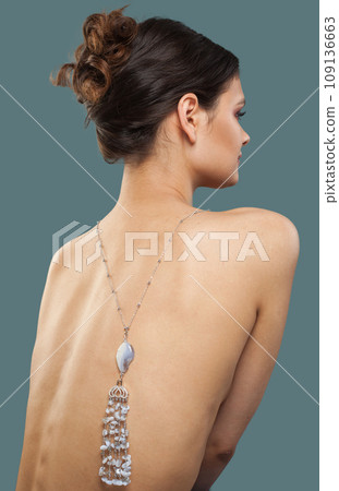 Attractive brunette female model with sautoir necklace on her back on blue background.  109136663