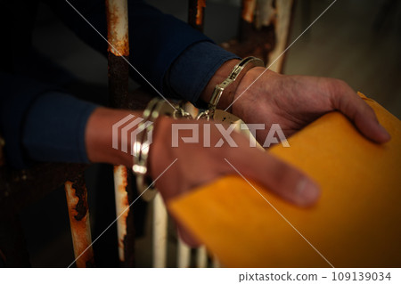 Asian businessmen hold documents and wear handcuffs in jail after arrest because corruption and defrauding insurance. Concept of punishment for crime fraudulent, victim criminal, justice protection. Asian businessmen hold documents and wear handcuffs in jail after arrest because corruption and defrauding insurance. Concept of punishment for crime fraudulent, victim criminal, justice protection. 109139034