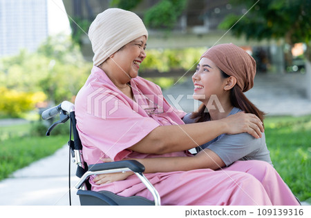 Asian careful caregiver or nurse and woman with cancer is sitting in a wheelchair. in the garden. Concept of happy retirement with care from a caregiver and Savings and senior health insurance. 109139316