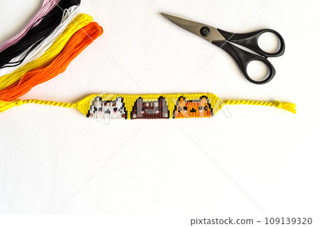 Woven DIY friendship bracelet with Cats pattern handmade of embroidery floss on white background. Woven DIY friendship bracelet with Cats pattern handmade of embroidery floss on white background. 109139320