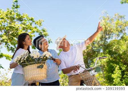 Happy and healthy Asian family standing beside a bicycle after workout together. friendship lifestyle, Enjoyment of active seniors, outdoor activity after retirement, health care insurance concept. Happy and healthy Asian family standing beside a bicycle after workout together. friendship lifestyle, Enjoyment of active seniors, outdoor activity after retirement, health care insurance concept. 109139393