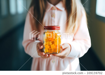 Schoolgirl child holds in her hands a jar of chewable gummy vitamins. The concept of taking vitamins to keep the child healthy while studying 109139702