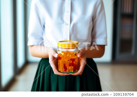 Schoolgirl child holds in her hands a jar of chewable gummy vitamins. The concept of taking vitamins to keep the child healthy while studying Schoolgirl child holds in her hands a jar of chewable gummy vitamins. The concept of taking vitamins to keep the child healthy while studying 109139704