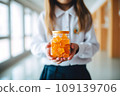 Schoolgirl child holds in her hands a jar of chewable gummy vitamins. The concept of taking vitamins to keep the child healthy while studying 109139706
