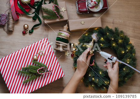 Top view of a woman using a glue gun to glue toys to a Christmas wreath. Holliday mood 109139785