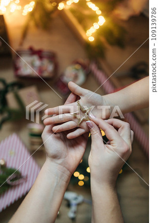 Mother put Christmas tree toy on daughter hand. Background of Christmas light and decorations. 109139786