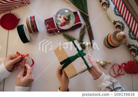 Top view of mom and daughter packing presents for Christmas Eve. Happy family spend time tougher on winter holidays Top view of mom and daughter packing presents for Christmas Eve. Happy family spend time tougher on winter holidays 109139816