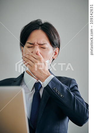 A male office worker wearing a mask covering his mouth with his hands 109142631