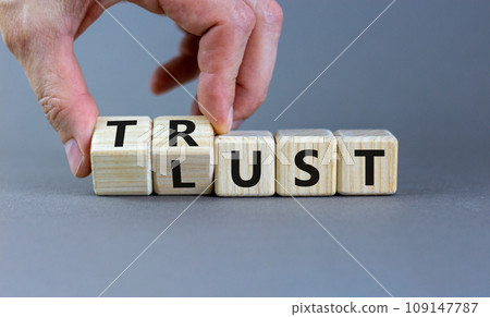 Lust or trust symbol. Businessman turns wooden cubes and changes the words 'lust' to 'trust'. Beautiful grey table, grey background. Business and lust or trust concept, copy space. 109147787