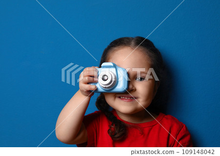 Little photographer taking picture with toy camera on blue background Little photographer taking picture with toy camera on blue background 109148042