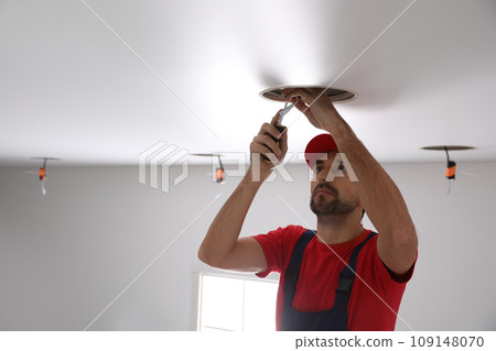 Worker installing lamp on stretch ceiling indoors 109148070