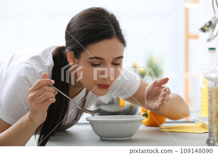 Young woman eating tasty vegetable soup at countertop in kitchen Young woman eating tasty vegetable soup at countertop in kitchen 109148090
