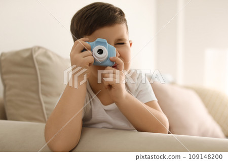 Little photographer taking picture with toy camera on sofa at home 109148200