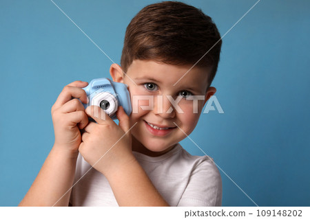 Little photographer with toy camera on light blue background 109148202