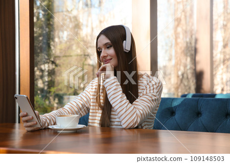 Woman listening to audiobook at table in cafe 109148503