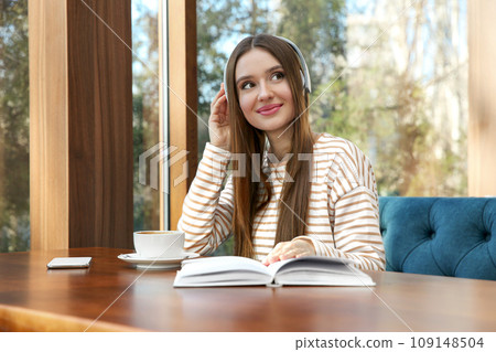 Woman listening to audiobook at table in cafe Woman listening to audiobook at table in cafe 109148504