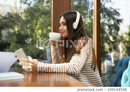 Woman listening to audiobook at table in cafe Woman listening to audiobook at table in cafe 109148506