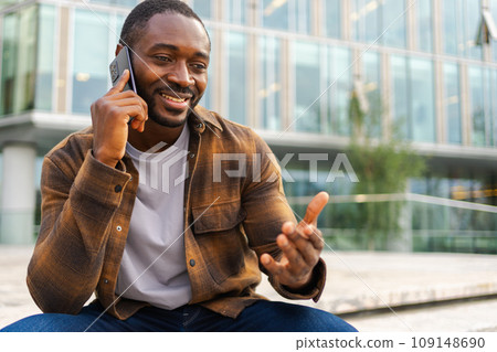 African american man talking on smartphone on street in city outdoor. Man with cell phone chatting with friends. Smiling person making answering call by cellphone. Guy having conversation by mobile 109148690
