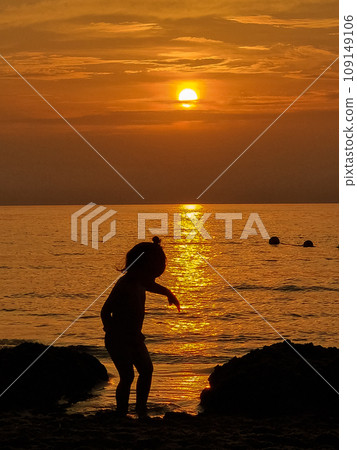 Silhouette of a little girl playing on the seashore during sunset 109149106