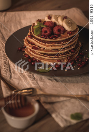 Pancakes with raspberries, banana slices, pomegranate seeds and honey Pancakes with raspberries, banana slices, pomegranate seeds and honey 109149516