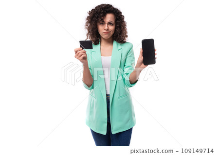 well-groomed young brunette curly businesswoman dressed in a blue jacket holds a plastic bank card 109149714