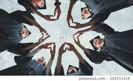 A group of college graduates stand in a circle and make hearts out of their palms. 109151419