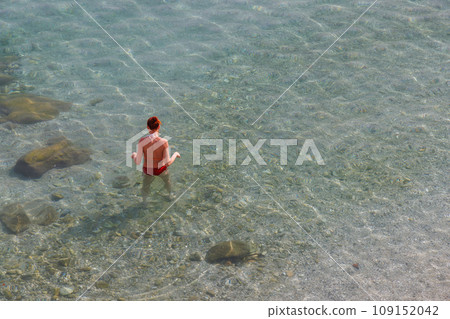 A woman stands waist-deep in the calm sea. She's wearing a red swimsuit. 109152042