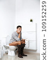 Man with paper roll sitting on toilet bowl in bathroom 109152259