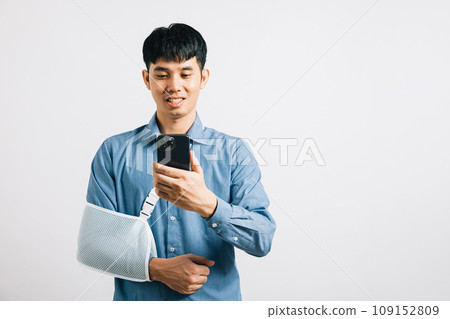 A man confidently smiles with a broken arm, using a splint, and holding a smartphone. An upbeat Asian woman with a sling-supported hand, isolated on white. Social media and copy space. 109152809