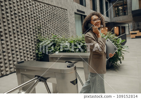 Smiling businesswoman is talking phone with client while standing on office background Smiling businesswoman is talking phone with client while standing on office background 109152814