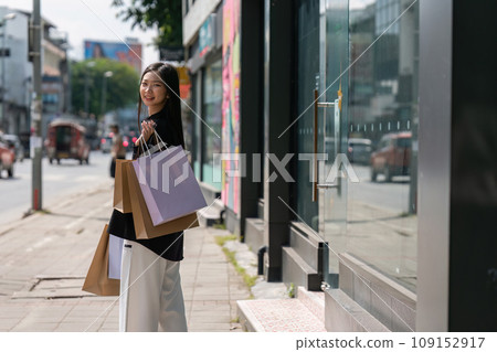 Young asian woman in shopping. Fashion woman in black with shopping bag walking around the city after shopping. Black friday Young asian woman in shopping. Fashion woman in black with shopping bag walking around the city after shopping. Black friday 109152917