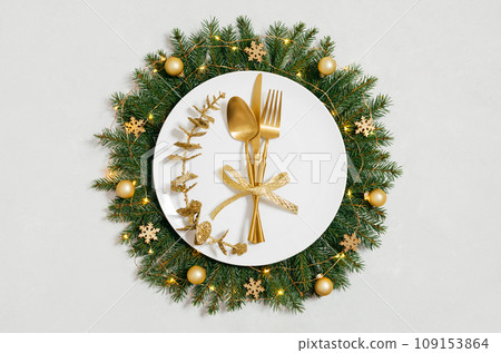 Beautiful Christmas table setting with gold cutlery, gold ornaments and festive wreath on white background. New Year party. Top view, flat lay. Beautiful Christmas table setting with gold cutlery, gold ornaments and festive wreath on white background. New Year party. Top view, flat lay. 109153864