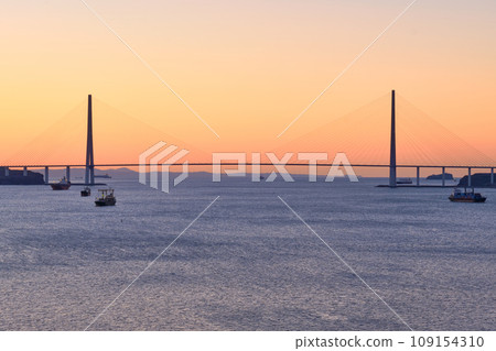 Suspended cable-stayed bridge from the mainland of the Far Eastern city to the Russian Island. The ships are in the roadstead in the Eastern Bosphorus Strait. Vladivostok, Russia. Suspended cable-stayed bridge from the mainland of the Far Eastern city to the Russian Island. The ships are in the roadstead in the Eastern Bosphorus Strait. Vladivostok, Russia. 109154310