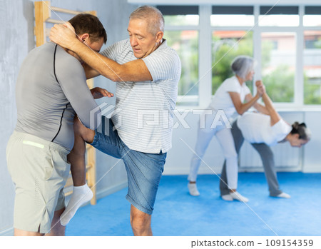 Mature man at self-defense lesson learns how to make painful blows with his hand and foot 109154359